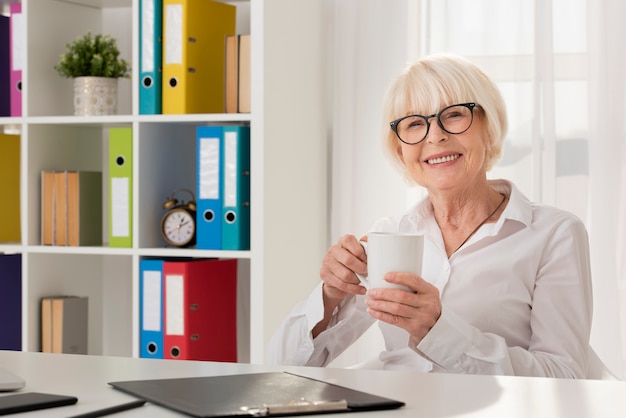 Foto gratuita smiley senior sosteniendo una taza en su oficina