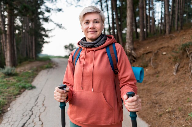 Smiley senior turista mujer con bastones de senderismo en el bosque
