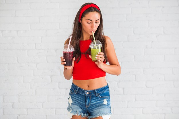 Smoothies de consumición de la mujer joven atractiva en taza plástica