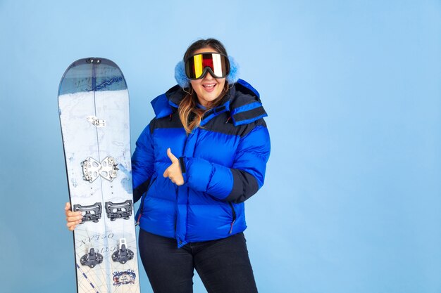 Snowboarding. Retrato de mujer caucásica en el espacio azul. Hermosa modelo de mujer en ropa de abrigo