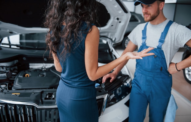 Sobre ese accidente. Mujer en el salón del automóvil con empleado en uniforme azul tomando su auto reparado