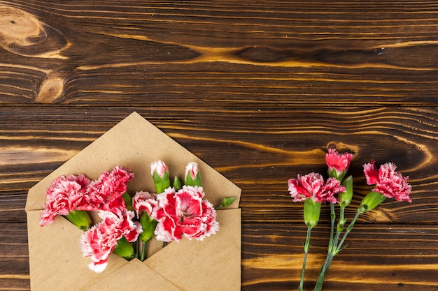 Sobre marrón y flores de clavel rojas en mesa de madera