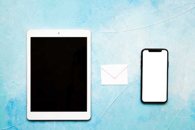 Sobre de papel blanco de iconos de mensaje con tableta digital y teléfono móvil sobre fondo azul pintado