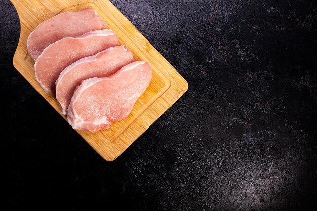 Sobre la vista superior de la carne cruda fresca en el tablero de madera sobre fondo de madera negra. Comida gourmet y comida fresca sin cocinar