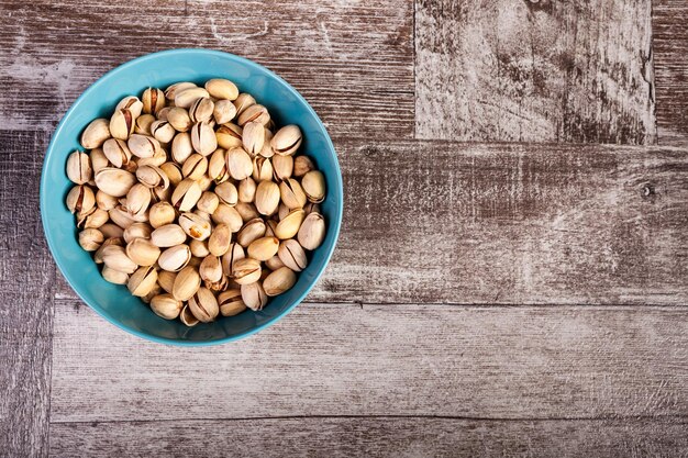 Sobre la vista superior de los pistachos en un tazón azul sobre fondo de madera en la foto de estudio. Bocadillos saludables y deliciosos