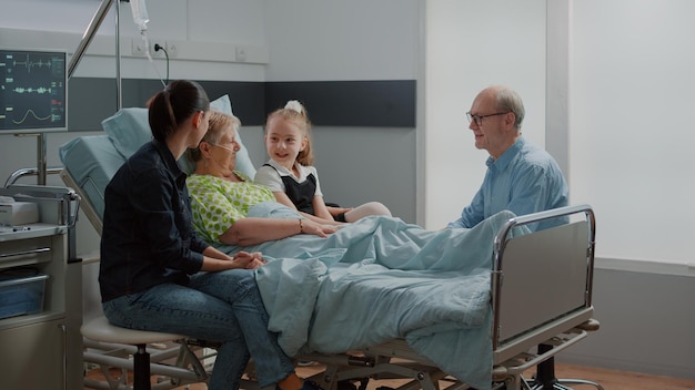 Sobrina abrazando a una mujer enferma en una visita familiar en la sala del hospital, niño y madre visitando a un paciente jubilado con enfermedad. Persona hospitalizada disfrutando del chat con una joven, ayudando con la recuperación.