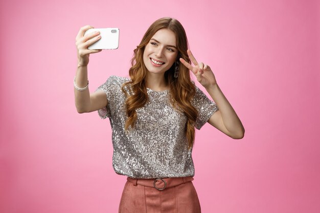 Sociable atractivo glamour joven mujer caucásica tomando selfie mostrar victoria signo de la paz sonriendo amplia ...