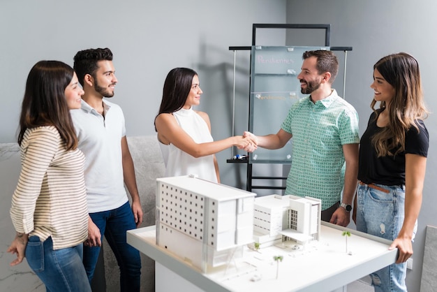 Foto gratuita socios comerciales estrechando la mano con el ingeniero por modelo arquitectónico en la reunión