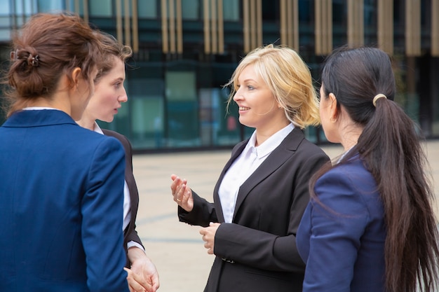 Socios comerciales femeninos discutiendo el trato al aire libre. Empresarias con trajes de pie juntos en la ciudad y hablando. Concepto de comunicación corporativa