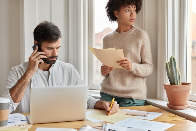 Los socios comerciales ocupados trabajan arduamente para obtener excelentes resultados. Hombre serio tiene conversación telefónica