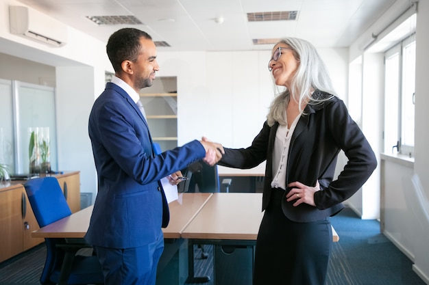 Socios seguros apretón de manos o saludo en la sala de reuniones. Empresario de contenido exitoso y gerente profesional canoso que concluye el contrato. Concepto de trabajo en equipo, negocios y asociación