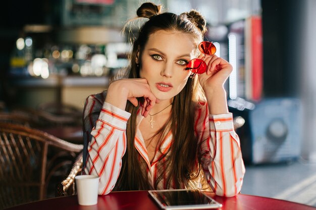 El sol brilla sobre las caras de la mujer imponente que se sienta con las gafas de sol rojas en el café