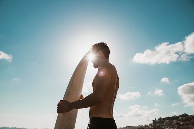 Sol brillante detrás de hombre con tabla de surf