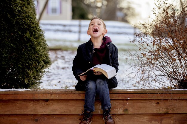 Sol sobre un lindo niño leyendo la Biblia en medio de un parque de invierno