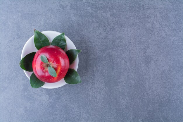 Una sola manzana en un recipiente sobre la superficie oscura.