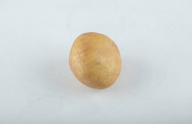 Una sola patata madura cruda sobre fondo blanco.