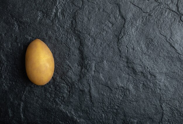 Una sola patata orgánica fresca sobre fondo de piedra negra.