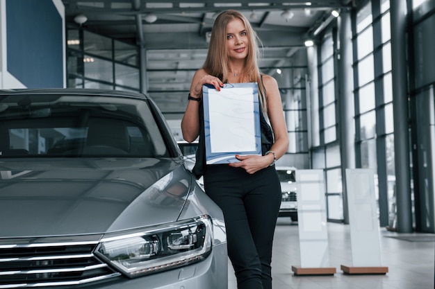 Una sola persona. Chica y coche moderno en el salón. Durante el día en interiores. Comprar vehículo nuevo