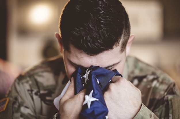 Soldado americano llorando y rezando con la bandera americana en sus manos