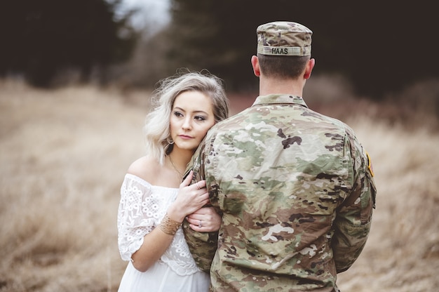 Foto gratuita soldado americano con su amada esposa de pie en un campo de hierba seca