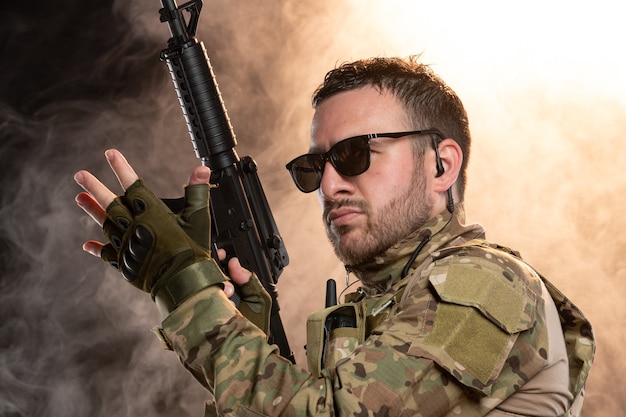 Foto gratuita soldado de camuflaje con ametralladora en pared ahumada