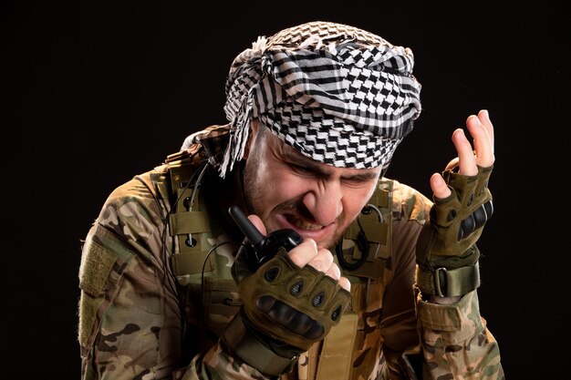 Soldado de camuflaje hablando a través de walkie-talkie en pared negra