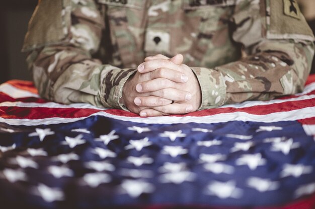 Soldado estadounidense llorando y rezando con la bandera estadounidense frente a él