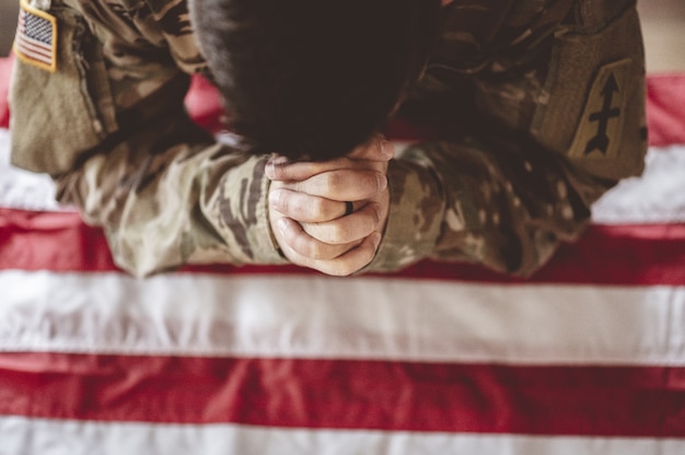 Soldado estadounidense llorando y rezando con la bandera estadounidense frente a él