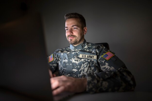 Soldado estadounidense en uniforme militar con banderas de parche de Estados Unidos trabajando hasta tarde en la computadora