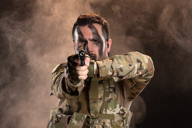 Soldado masculino en camuflaje con el objetivo de pistola en la oscura pared ahumada