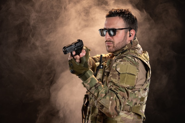 Soldado masculino en camuflaje con el objetivo de pistola en la pared oscura