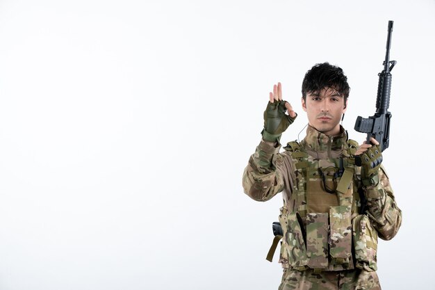 Soldado masculino de vista frontal con ametralladora en pared blanca de camuflaje