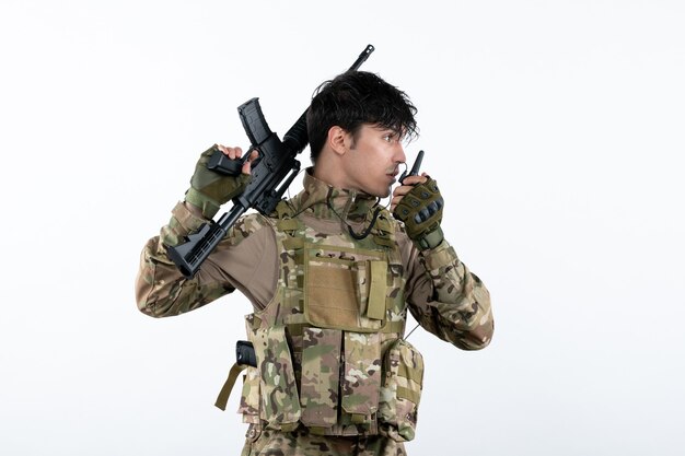 Soldado masculino de vista frontal hablando a través de walkie-talkie en pared blanca de camuflaje