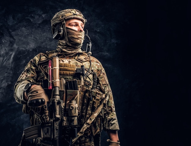 Soldado moderno de las fuerzas especiales con uniforme de camuflaje mirando hacia los lados. Foto de estudio contra una pared de textura oscura.