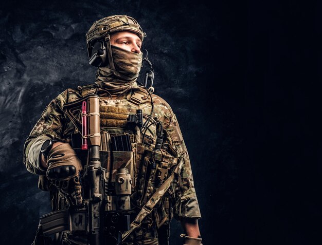 Soldado moderno de las fuerzas especiales con uniforme de camuflaje mirando hacia los lados. Foto de estudio contra una pared de textura oscura.