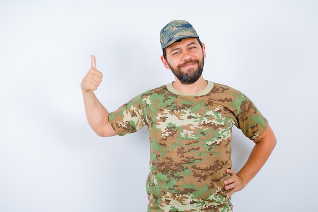 El soldado sonriente está mostrando un gesto perfecto y poniendo otro en la cintura sobre fondo blanco.