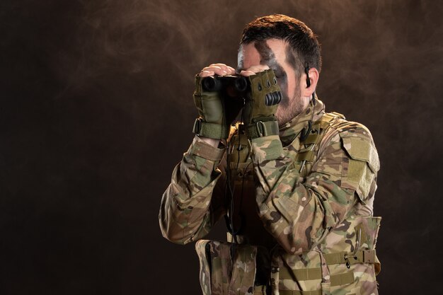 Soldado en uniforme militar con binoculares en la pared oscura