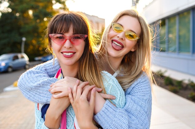 Soleado retrato positivo de la feliz pareja de lesbianas disfrutando de tiempo juntos, colores soleados, moda trajes pastel y gafas de sol, primavera otoño, felices vacaciones en Europa.