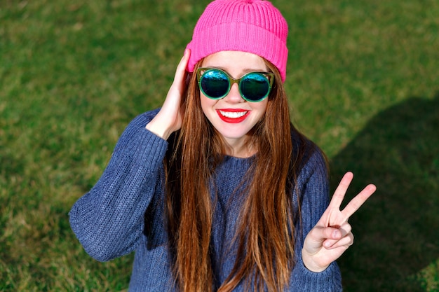 Soleado retrato positivo de feliz sonriente hipster mujer, posando en el parque, viajes, vacaciones, alegría, muestra v por sus buscadores, humor primaveral, suéter y sombrero.