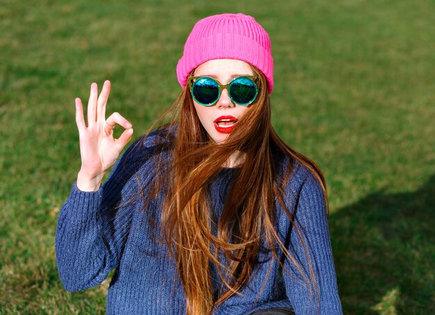 Soleado retrato positivo de feliz sonriente hipster mujer, posando en el parque, viajes, vacaciones, alegría, muestra v por sus buscadores, humor primaveral, suéter y sombrero.