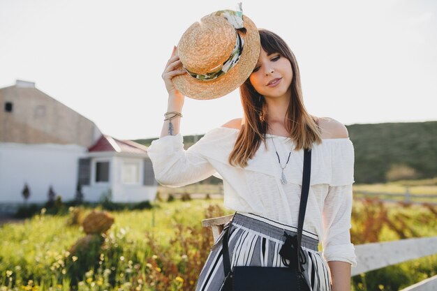 Soleado retrato de sonriente joven hermosa mujer elegante, tendencia de moda primavera verano, estilo boho, sombrero de paja, fin de semana de campo, bolso negro soleado