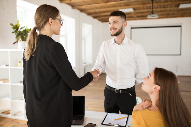 Solicitante masculino alegre felizmente estrechando la mano del empleador Joven hombre guapo con camisa blanca que consigue un nuevo trabajo después de una entrevista en una oficina moderna