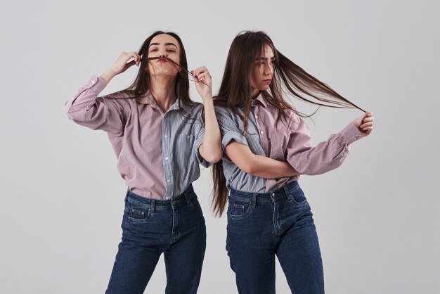 Solo bromeando. Dos hermanas gemelas de pie y posando en el estudio con fondo blanco.