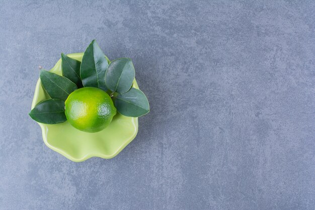 Un solo limón con hojas en un recipiente sobre una mesa de mármol.