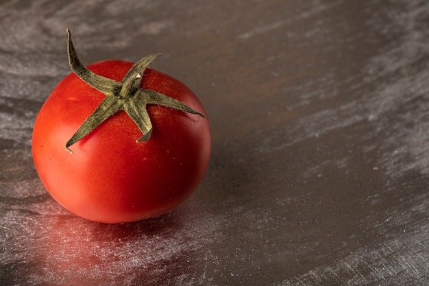 Un solo tomate rojo sobre un fondo metálico plateado.