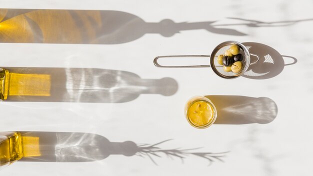 Sombra de la botella de aceite con aceitunas en el colador de té sobre fondo blanco