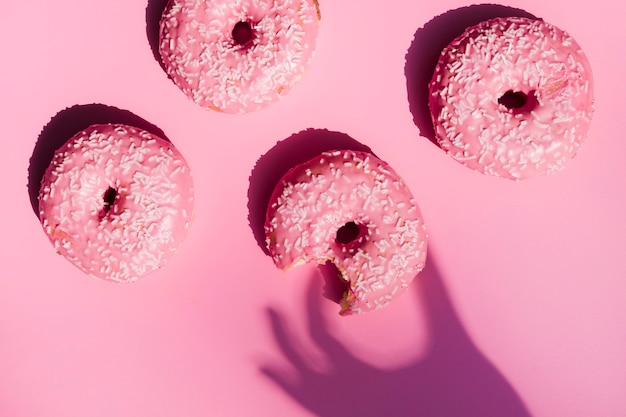 Sombra de la mano de una persona cerca de los donuts comidos contra el fondo rosa