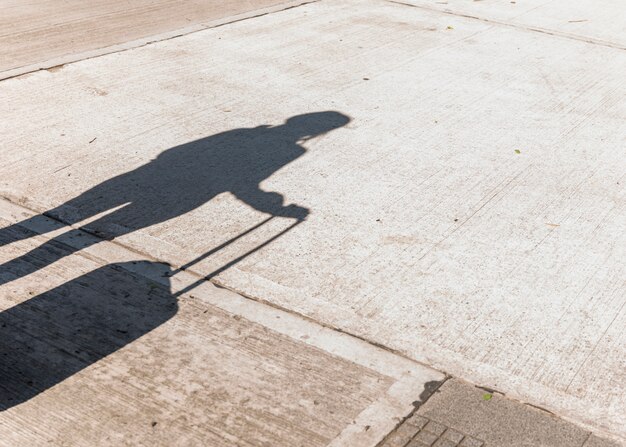 Sombra de una mujer turista con equipaje de ruedas sobre asfalto