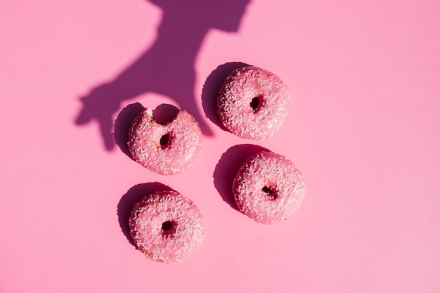 Foto gratuita sombra de una persona cerca de los donuts sobre fondo rosa