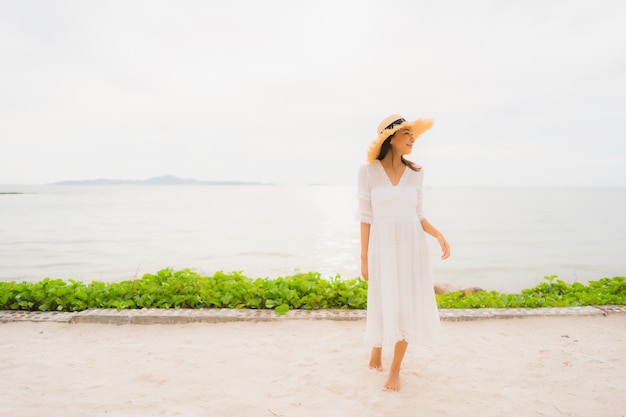 Sombrero asiático hermoso del desgaste de mujer del retrato con ocio feliz de la sonrisa en la playa y el mar en vacaciones del día de fiesta